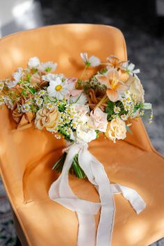 a bouquet of flowers sitting on top of an orange chair with white ribbon around it