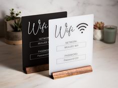 two black and white signs sitting next to each other on top of a table with succulent plants