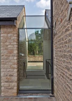 an open door leading to a hallway with brick walls and doors on both sides, in front of a stone building