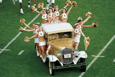 a group of cheerleaders standing on the back of a car in front of a football field