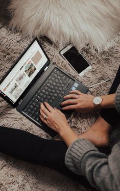 a woman is sitting on the floor with her laptop and cell phone in front of her