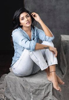 a woman sitting on the ground with her legs crossed and looking at the camera while wearing jeans