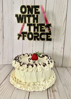 a white cake sitting on top of a wooden table next to a sign that says, one with the force