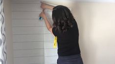 a woman is painting the wall with white paint on it and she's holding a yellow tape