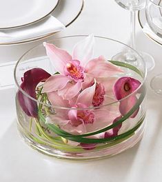 a glass bowl filled with pink flowers on top of a white tablecloth covered table