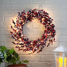 a wreath with red, white and blue beads hanging on a brick wall next to a lamp