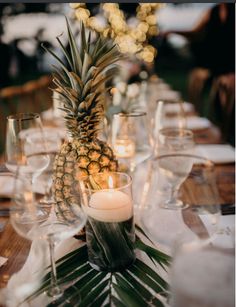 a pineapple is sitting on top of a table with wine glasses and candles in front of it