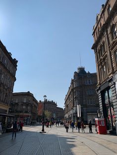 people are walking down the street in front of buildings and shops on a sunny day