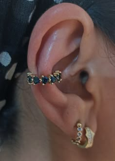 a woman wearing three different ear piercings on her left ear, and one with blue stones in the middle