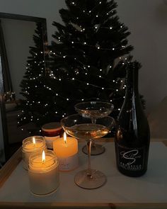 candles and wine are sitting on a table next to a christmas tree with a lit candle in front of it