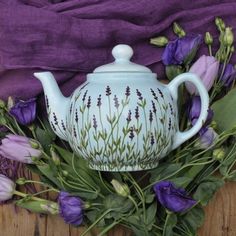 a tea pot with purple flowers in it on a wooden table next to a purple cloth