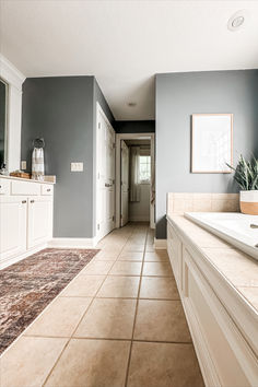 a large bathroom with tile flooring and white cabinetry, along with an area rug on the floor