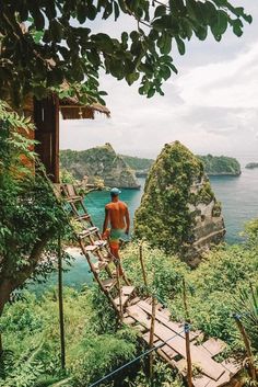 a man walking across a wooden bridge near the ocean with green vegetation on both sides