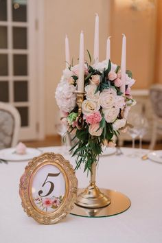 an arrangement of flowers and candles in a vase on a table at a wedding reception