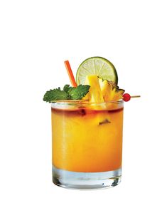 a tall glass filled with orange juice and garnished with pineapple, lime, and mint