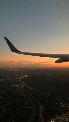 the wing of an airplane as it flies over a city at sunset or dawn with lights on