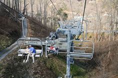 two people sitting on a chair lift in the woods