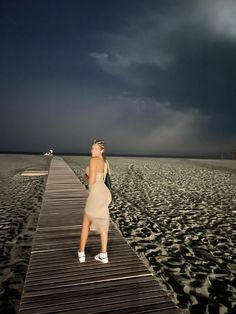 a woman is standing on a dock at the beach looking up into the dark sky