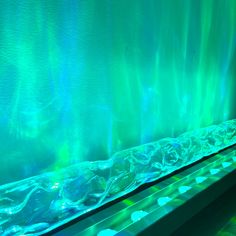 an aquarium filled with lots of water next to a long wall covered in green and blue lights