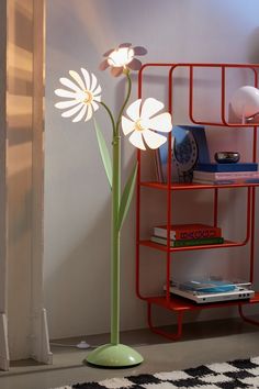 a lamp that is next to a book shelf with books on it and a flower in the middle