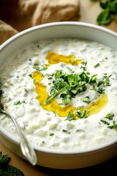 a white bowl filled with soup and topped with cucumber, parsley and mustard