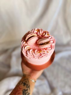 a hand holding a pink frosted donut with gold sprinkles on it