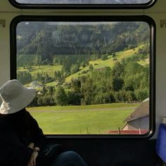 a person sitting on a train looking out the window at mountains and trees in the distance