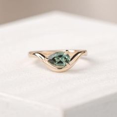 a gold ring with a green stone in the middle on top of a white box