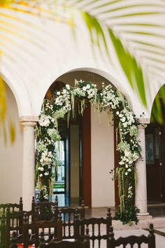 an archway decorated with white flowers and greenery is shown in front of a building