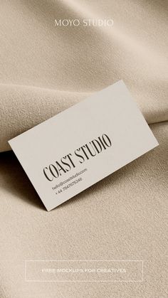 a white business card sitting on top of a beige fabric covered bed sheet with the words coast studio printed on it