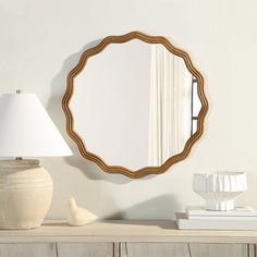 a mirror sitting on top of a wooden table next to a white vase and lamp