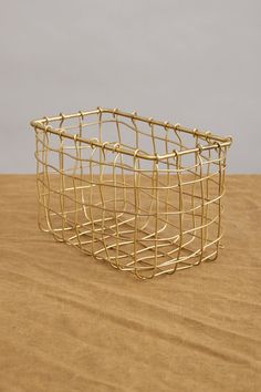 a gold wire basket sitting on top of a wooden table next to a white wall