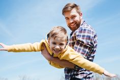 a man holding a little boy in his arms and smiling at the camera with blue sky behind him