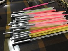 many different colored straws are lined up on a table next to glasses and pens