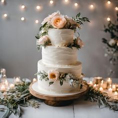 a wedding cake with flowers and greenery sits on a table surrounded by lit candles