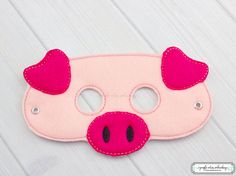 a pink pig mask with red ears and eyes on a white wooden surface, ready to be sewn