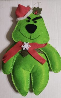 a green teddy bear with a red ribbon around it's neck and wearing a santa hat