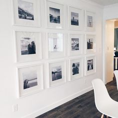 a dining room table with white chairs and pictures on the wall behind it in black and white