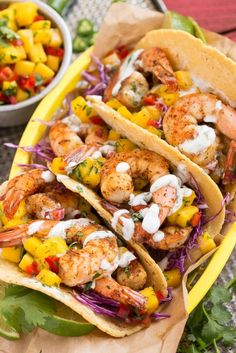 three tacos with shrimp, pineapple and mango salsa in them on a yellow plate