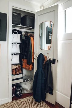 an open closet with clothes hanging on hooks, and a mirror over the door above it