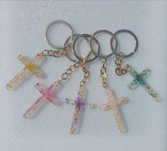 six cross shaped key chains are shown on a white surface, one is multicolored and the other is silver