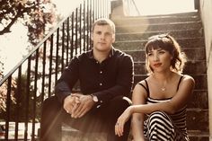 a man and woman sitting on the steps next to each other in front of some stairs