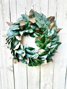 a wreath made out of green leaves on a white fence with the words, how to make a paper wreath