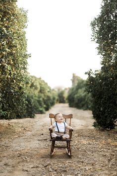 a baby sitting in a wooden chair on a dirt road