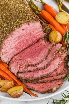 a white plate topped with meat, carrots and potatoes next to some rosemary sprigs