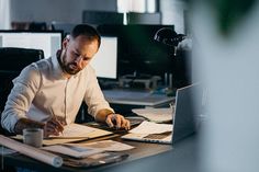 a man sitting at a desk working on his laptop and writing something in front of him