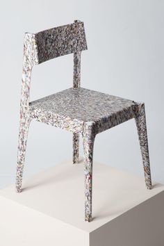 a chair made out of paper sitting on top of a white platform in front of a gray wall