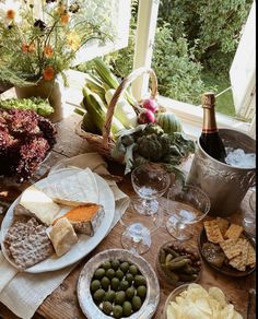 a wooden table topped with plates and bowls filled with food next to a bottle of wine