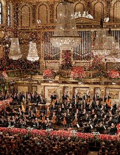 an orchestra performing in front of a large crowd with christmas decorations on the ceiling and chandelier