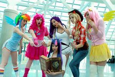 four women dressed in costumes posing for the camera with one holding a book and two wearing colorful wigs